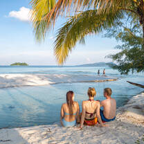 three girls sitting on the beach facing the ocean
