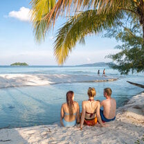 three girls sitting on the beach facing the ocean