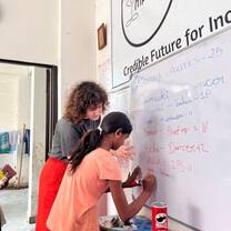 a teacher helping a young girl write on a whiteboard