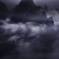 Dark clouds gather at the base of a moody mountain