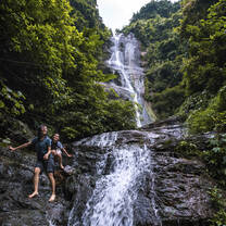 Two girls walk bare foot near a waterfall