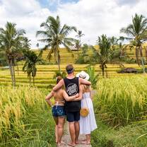man facing away from camera with his arms around two woman in front of a rice field