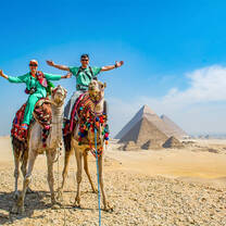 two people on camels with Egyptian pyramids in the background
