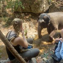 a girl sits next to a baby elephant