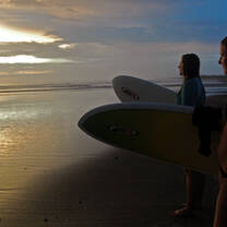 Two girls holding their surfboards, during sunset headed towards the ocean in Costa Rica.