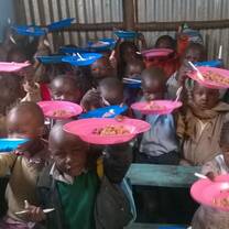 young children sitting on benches holding up pink and blue plates with food 