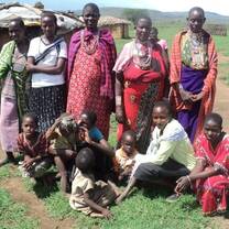 group of girls posing for a photo in the grass in front of a hut