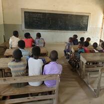 students sitting on benches in a classroom facing a blackboard