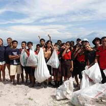 A group of interns, staff, and local school children posing on the beach with the trash they have collected together