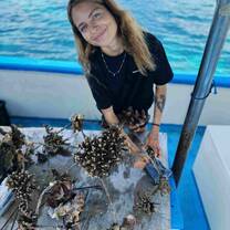 A Happy intern on the boat attaching coral fragments to a metal coral structure while smiling at the camera