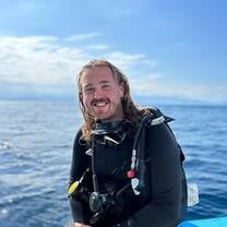 A happy male diver sitting on the edge of the dive boat in full gear smiling at the camera