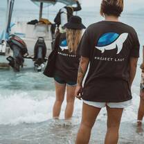 A shot of two female divers wearing project laut t shirts with the turtle logo on the backs waiting to board the dive boat