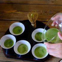 hands pouring green matcha into five small cups