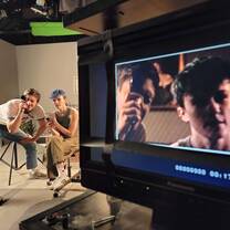 Two students sitting together on a film set with a close-up of their faces on a monitor