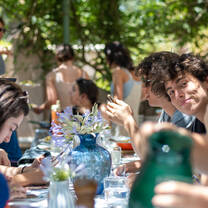 LITA students sit together at a long table, painting their individual traditional ceramic pots, laughing and smiling. One student in the group smiles at the camera
