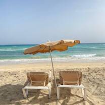 Two lounge chairs under a beach umbrella facing the turquoise waves of a sandy Spanish beach, capturing the serene and relaxing coastal experiences available to RVF International participants while teaching abroad in Spain.