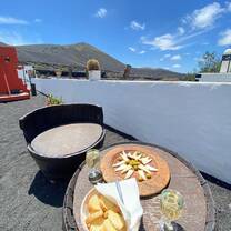 A table set with Spanish wine, cheese, olives, and bread against a backdrop of volcanic hills and a clear blue sky, showcasing the rich flavors and relaxing moments participants enjoy with RVF International’s Teach English in Spain program.