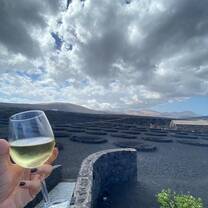 Glass of white wine held before stunning volcanic vineyards and dramatic skies in Spain, highlighting the country’s breathtaking wine landscapes.