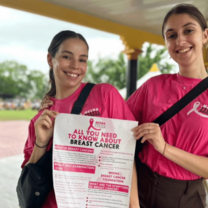 Two volunteers wearing pink t-shirts hold up information regarding breast cancer