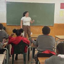 A volunteer stands in front of a chalkboard, addressing a classroom