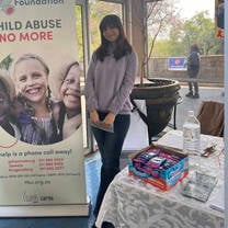 A volunteer in South Africa stands at a table stall with a banner that reads 'Child Abuse No More'
