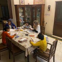 A volunteer sits at a table with children. They all have their heads down, working hard, while the volunteer helps them.