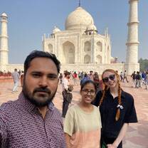 Two volunteers stand with their volunteer coordinator, smiling in front of the Taj Mahal