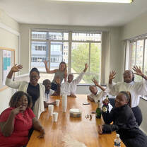 A group of people gathered around a table wave at the camera