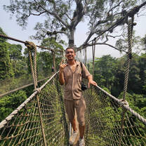A volunteer stands smiling on a rope bridge, high above the canopy of Ghana's Kakum Forest