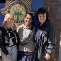 Two volunteers stand outside of a police station in South Africa with their volunteer coordinator