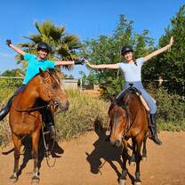 Two volunteers having fun on horse back arm stretched out 