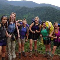 Crew poses for picture on a red dirt trail against background of lush mountain valley.