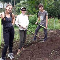 Three students pose for a picture holding gardening tools as they work on a service project.