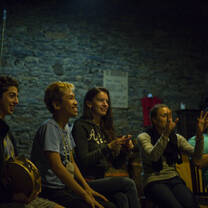 Five people (students and group leaders) sitting in a large room, singing and playing tamborines
