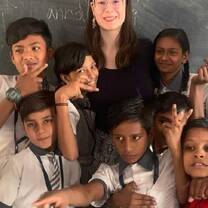Intern posing with a group of smiling schoolchildren in a classroom in Jaipur, India.