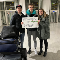 International student arriving in Spain, warmly welcomed by his host family at the airport with a sign saying "Welcome to La Rioja".