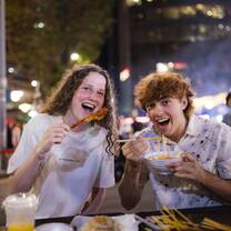 EF Gap Year students enjoying Japanese street food in Tokyo at night, laughing together while trying local dishes like ramen and skewers under the city lights.