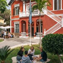 EF Gap Year students relaxing and chatting on the lawn of the EF Málaga campus, surrounded by palm trees and the school’s vibrant red architecture on a sunny afternoon.