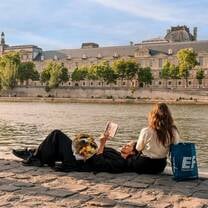 EF Gap Year students relaxing by the Seine River in Paris, reading and enjoying the sunshine with the Louvre in the background—embracing culture and connection during their time abroad.