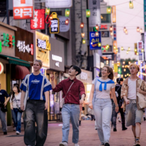 Group of EF Gap Year students walking through a bustling street in Seoul, South Korea at dusk, with colorful neon signs and hanging lanterns above.