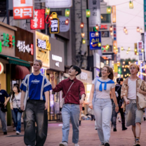Group of EF Gap Year students walking through a bustling street in Seoul, South Korea at dusk, with colorful neon signs and hanging lanterns above.