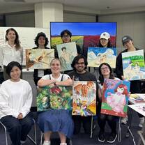 A group of CET Japan students and teachers holding up their artwork while in a classroom