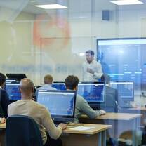 A professor delivers a lecture to students sat in front of computers in a trading simulation lab.