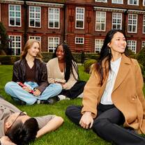 A group of students sitting on a green lawn smiling and talking.