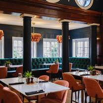 A restaurant with a collection of white tables, peach-coloured chairs, deep green accent columns and deep green painted and wood walls. 
