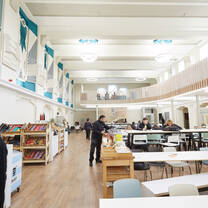 A bright and spacious two-floor cafeteria with a high ceiling, oak accents and rows of tables and chairs.