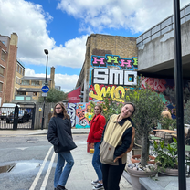 Three girls smiling on a street with graffiti walls in the UK