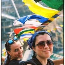 Two smiling students stand in front of prayer flags 