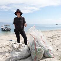 A project laut intern posing behind the bags of trash she collected on the beach