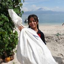 A young Indonesian schoolgirl holding up a bag of trash she collected from the beach